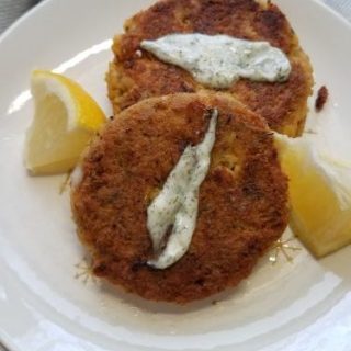 two salmon cakes on plate with lemon wedges