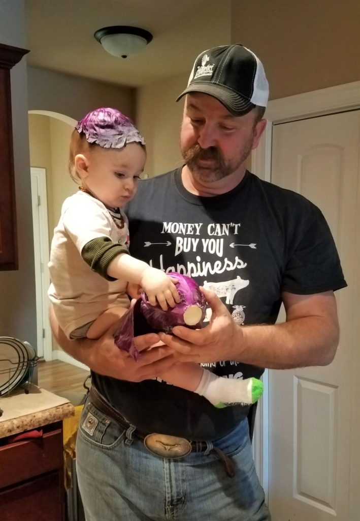 Man holding toddler with red cabbage leaf on head