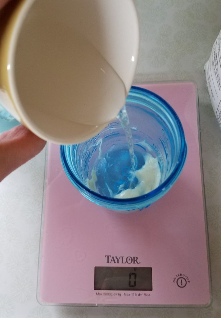 water being poured into a small sourdough starter in blue jar