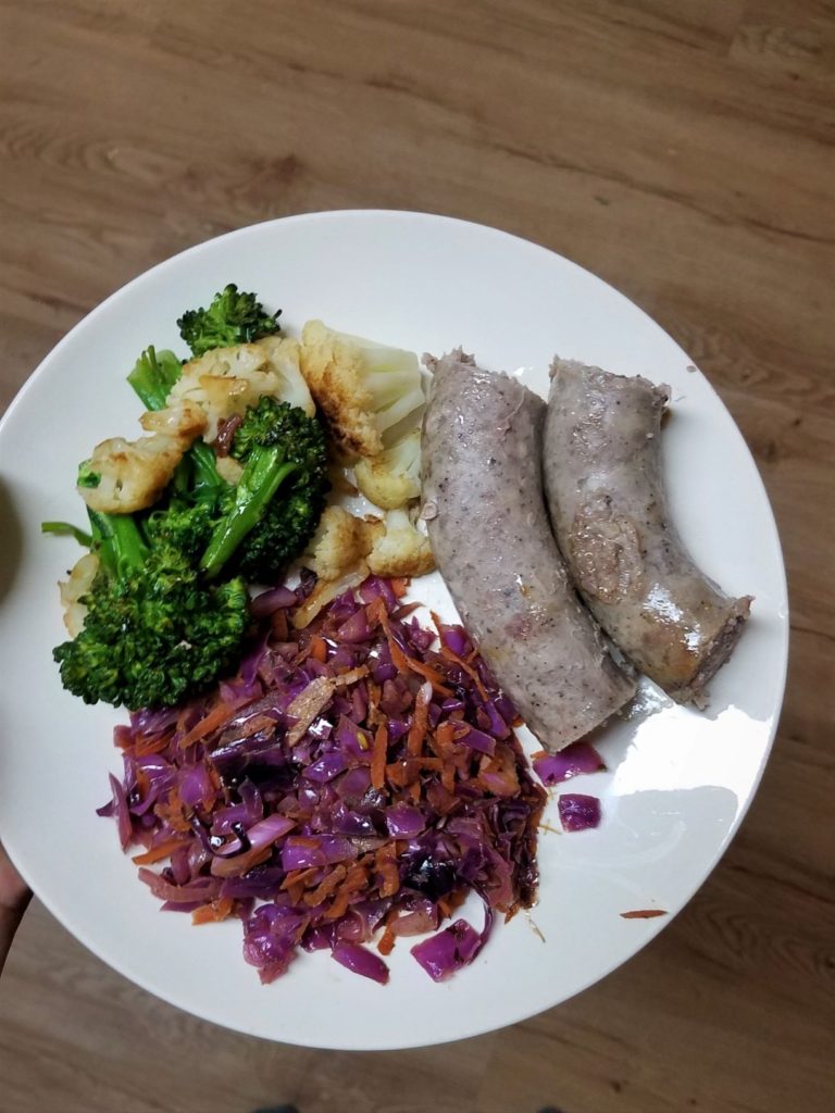 Sautéed red cabbage, steamed brocolli & cauliflower, and pork sausage on a white plate
