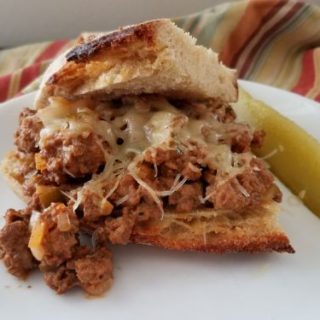 spicy sloppy joe on plate with pickle, striped towel in background