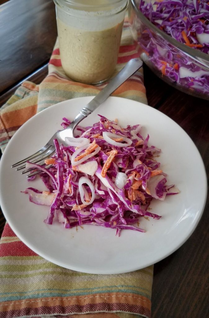 creamy coleslaw on plate on striped towel with dressing in jar