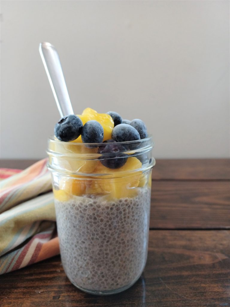 Dairy-free chia pudding topped with mangos and blueberries in mason jar with spoon