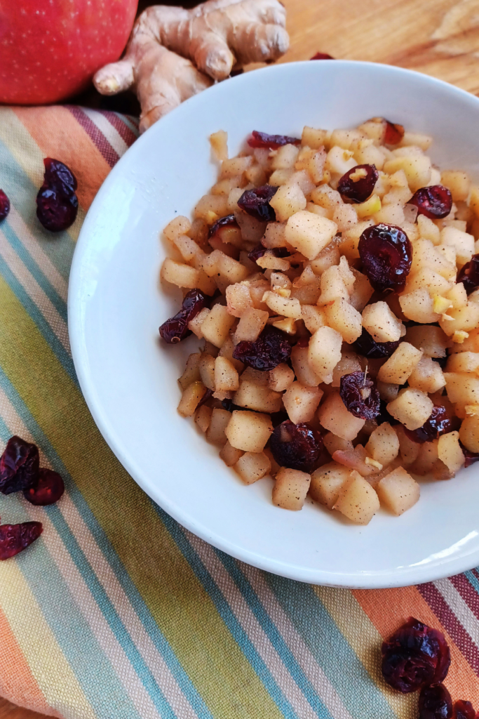 Apple Chutney in bowl on striped towel with apple, ginger and cranberries around