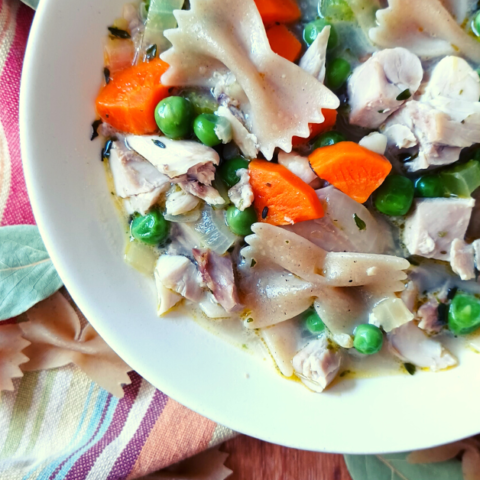 Homemade chicken noodle soup in white bowl on stripped towel