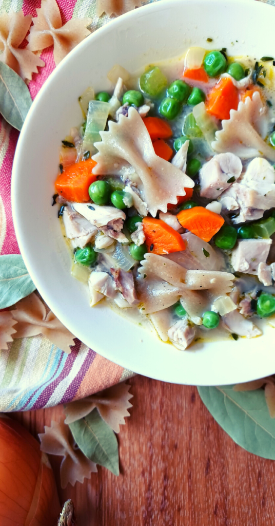 Homemade chicken noodle soup in white bowl on stripped towel