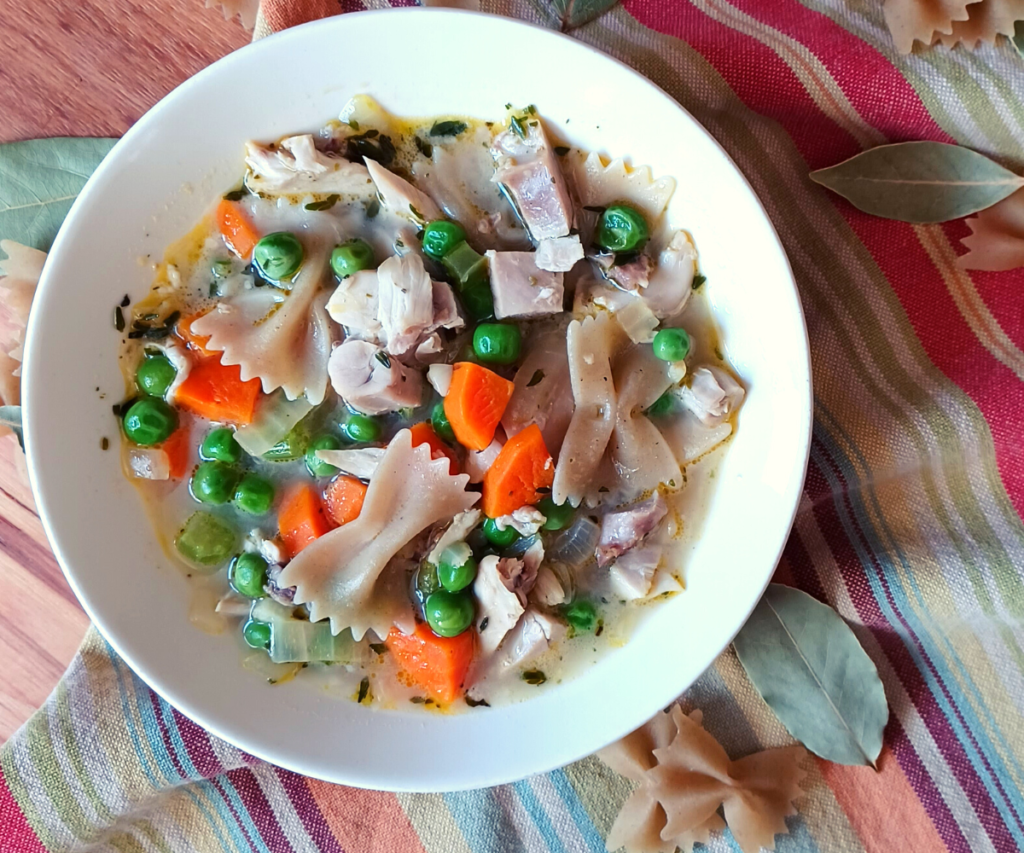 Homemade chicken noodle soup with gluten-free bowtie pasta in bowl on tea towel.