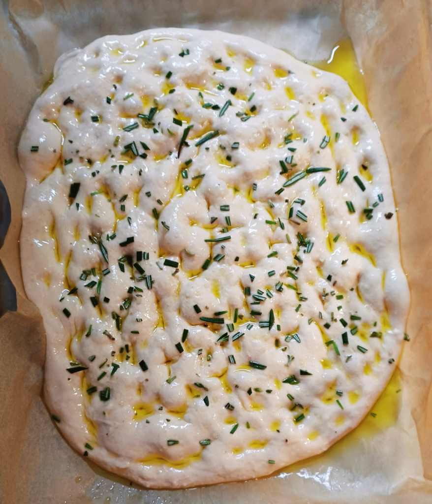 Sourdough focaccia dough dimpled and topped with salt  and rosemary