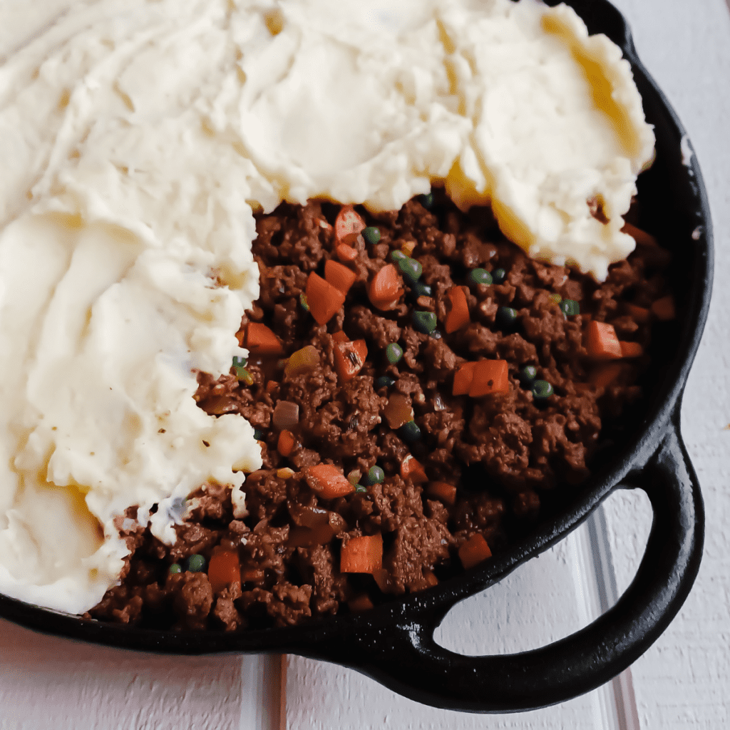 cottage pie partially topped with mashed potatoes during the assembly process