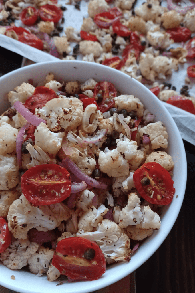 Roasted cauliflower with capers, tomatoes, and onions in white bowl.