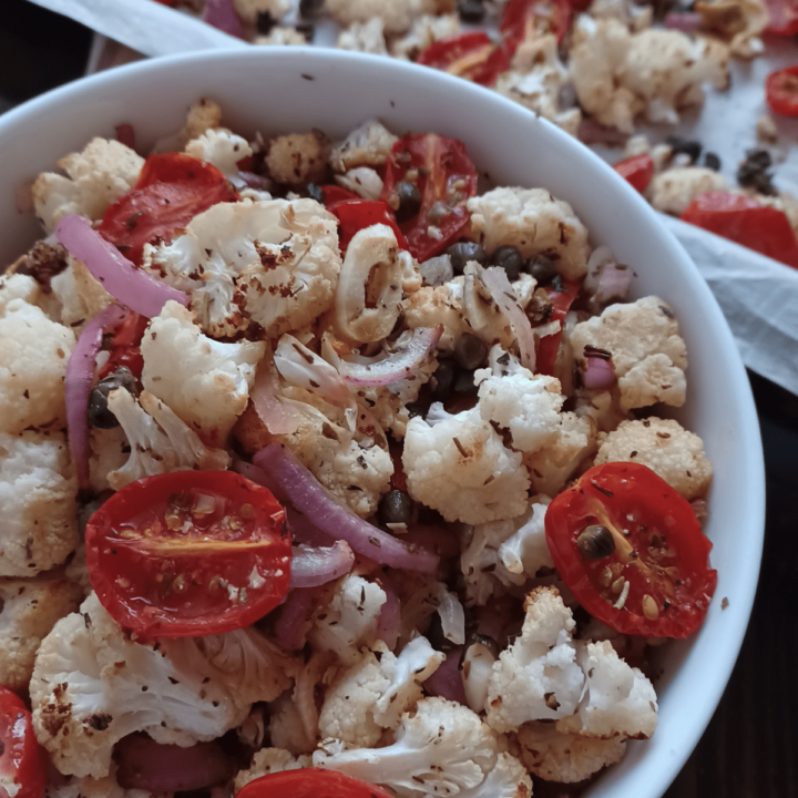 Roasted cauliflower with capers, tomatoes, and onions in white bowl.