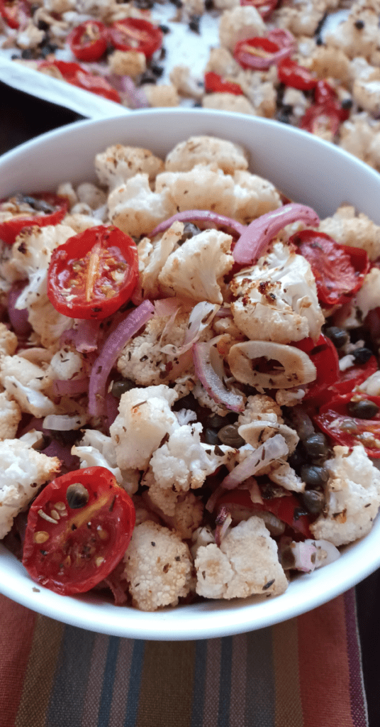 White bowl filled with oven roasted cauliflower with capers, tomatoes, and red onion.