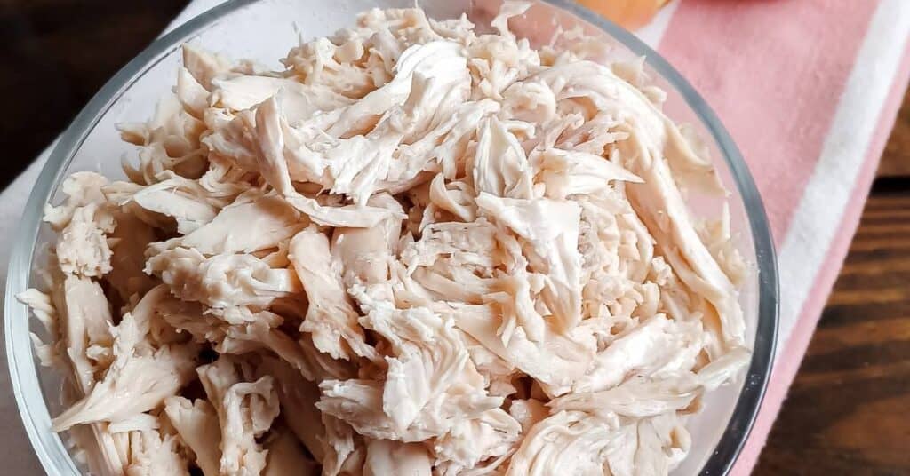 glass bowl of shredded chicken on a white and red towel