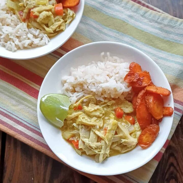Chicken curry with cocnut milk in a bowl with white rice, carrots, and a lime wedge
