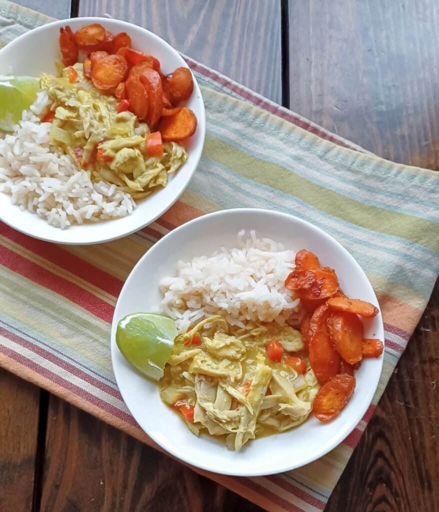 Two bowls filled with rice, roasted carrots, and creamy chicken curry on a striped towel.