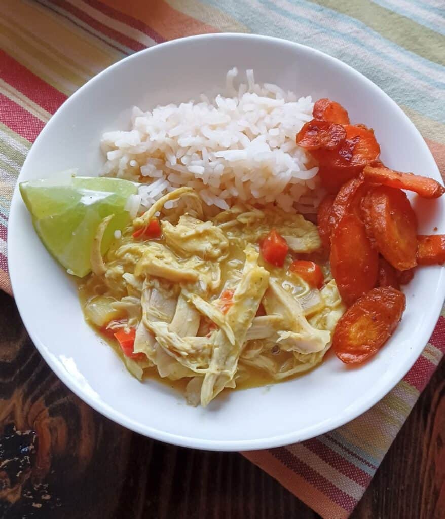 white bowel containing chicken curry with coconut milk, white rice, roasted carrots & a lime wedge