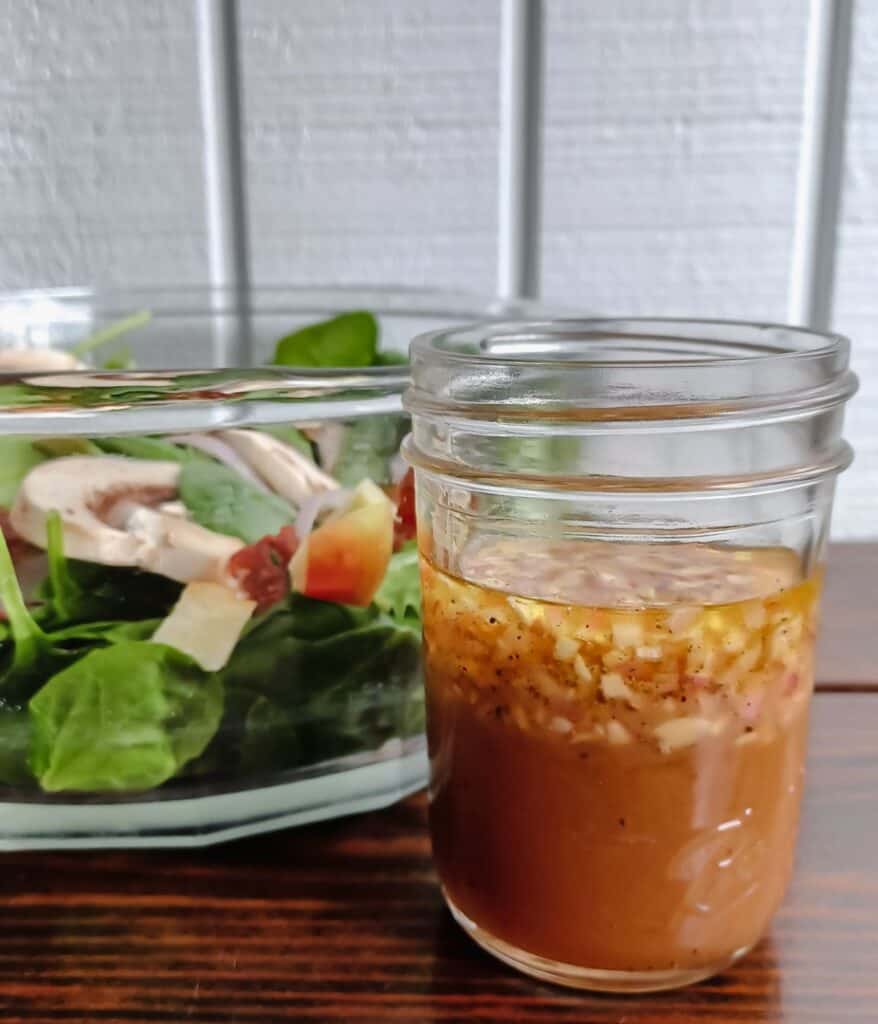 Maple-Dijon vinaigrette in mason jar sitting in front of a bowl of spinach salad.