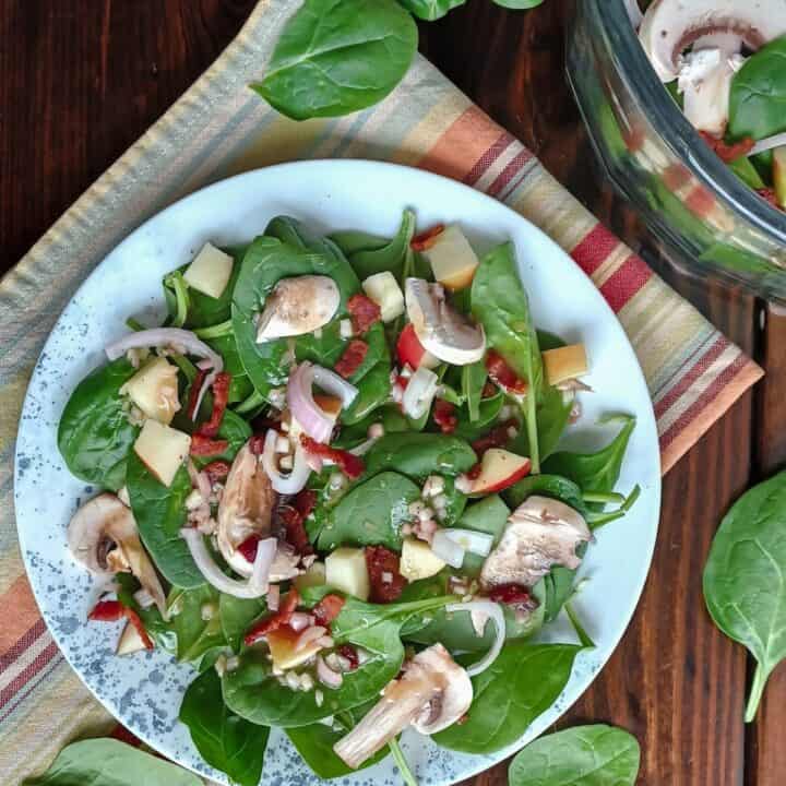 Spinach salad on a plate with blue dots and in a large glass serving bowl