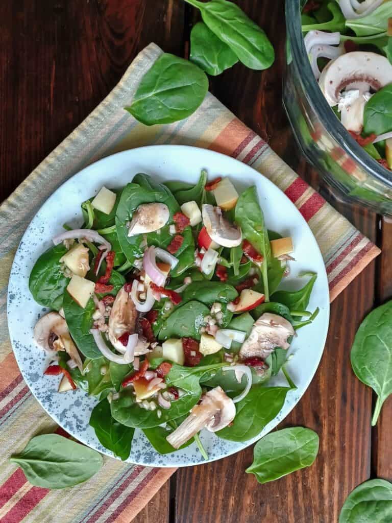 Spinach salad on a plate with blue dots and in a large glass serving bowl