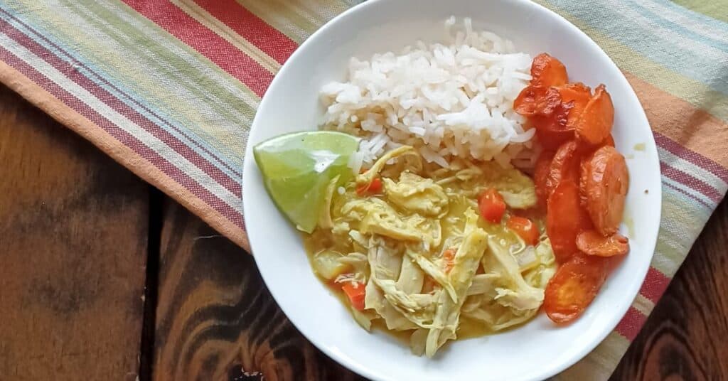 Rice, carrots and chicken curry in white bowl on a striped towel