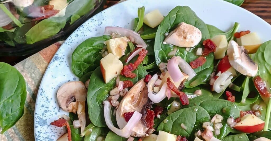 spinach salad with bacon, apples, shallots, and mushrooms on a plate with maple-Dijon vinaigrette