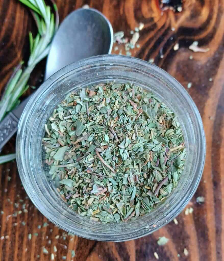 Italian herb blend in mason jar with spoon and rosemary springs