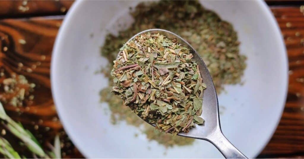 Italian Herb Blend on a spoon with rosemary springs and bowl of herbs in background