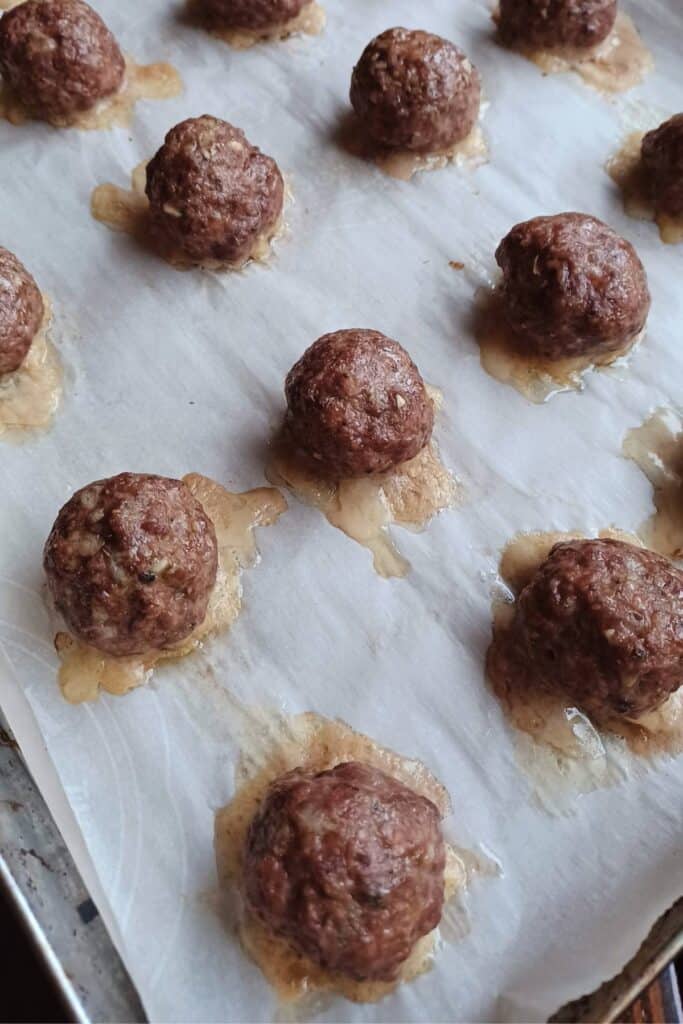 Baked homemade meatballs on a baking sheet lined with parchment paper