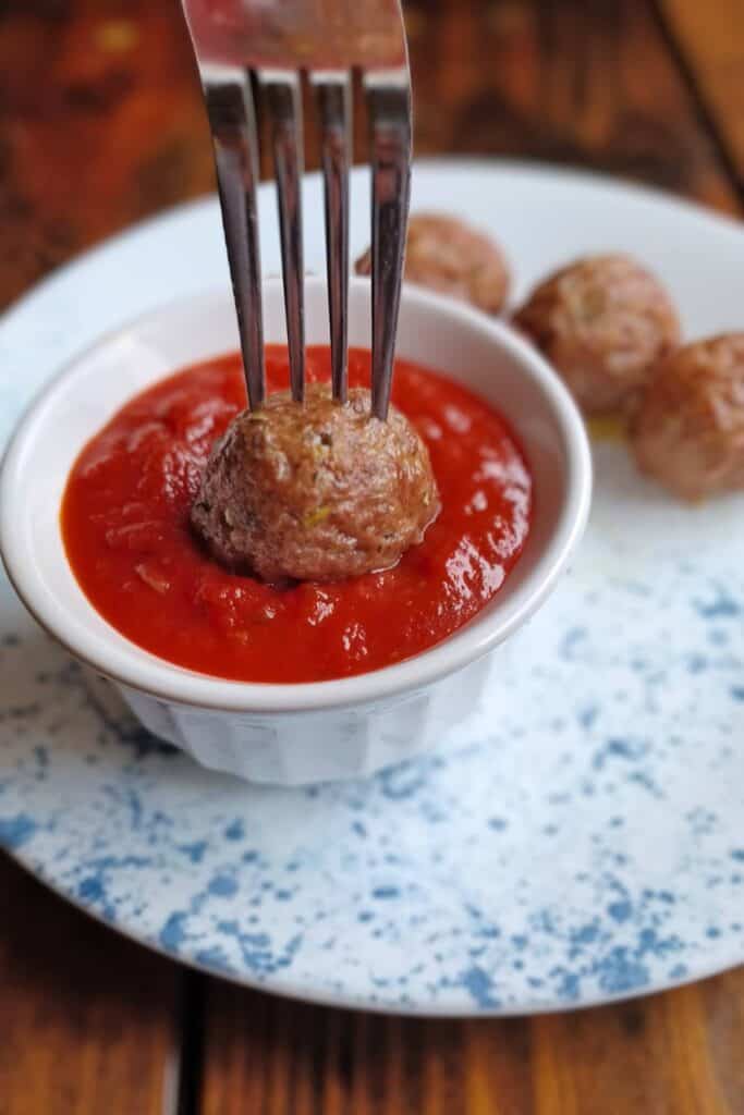 homemade meatballs on a fork being dipped into tomato sauce