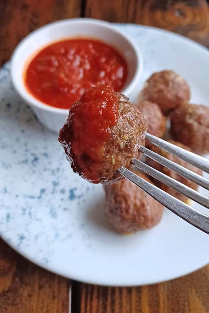 fork with meatball on it that has been dipped in tomato sauce.