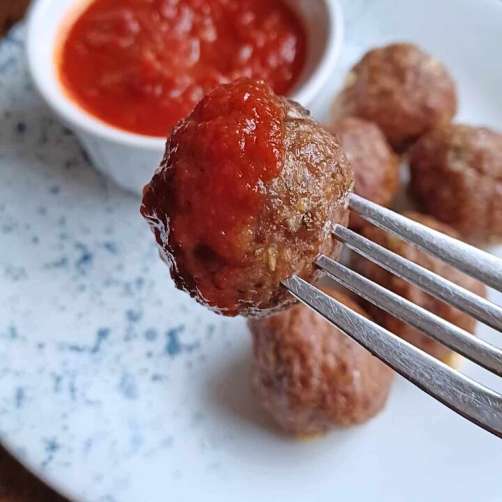 fork with meatball on it that has been dipped in tomato sauce.