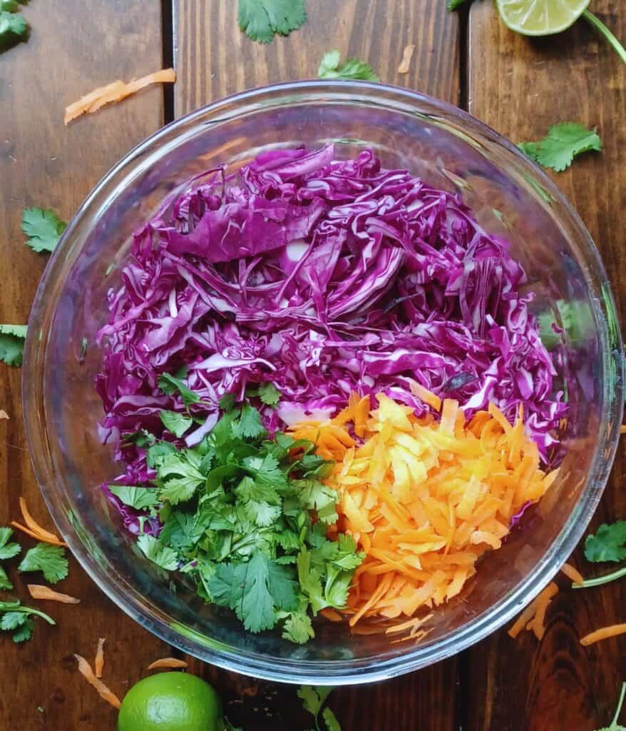 shredded red cabbage, shredded carrots, and chopped cilantro in a large glass bowl