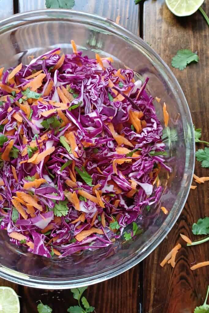 Shredded cabbage and carrots, and chopped cilantro for cilantro lime slaw in a glass bowl