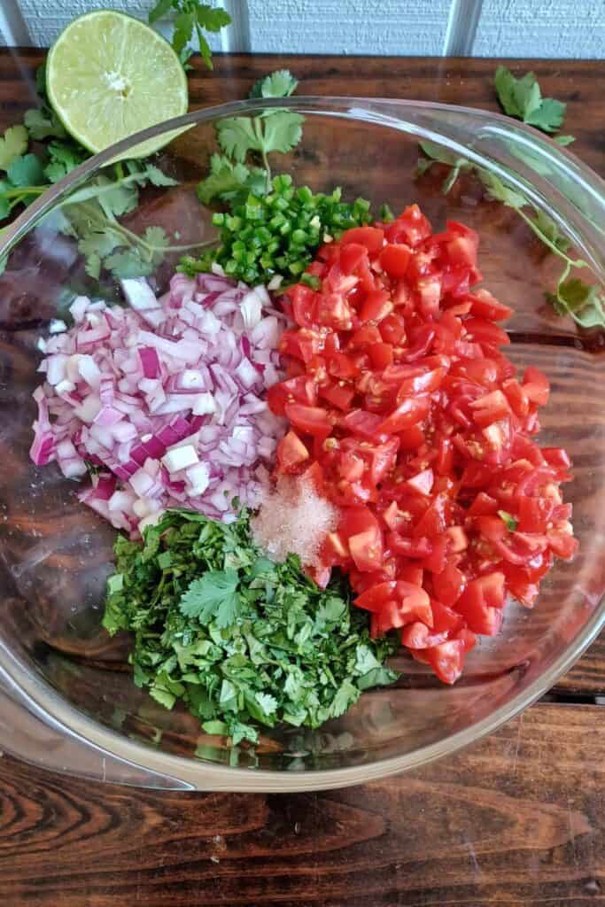 Chopped jalapeno, cilantro, red onion, and tomatoes in a glass bowl.