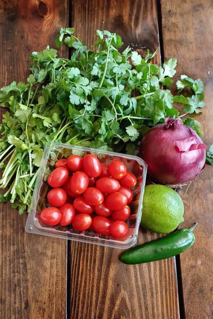 Cilantro, red onion, lime, jalapeno, and cherry tomatoes on a table