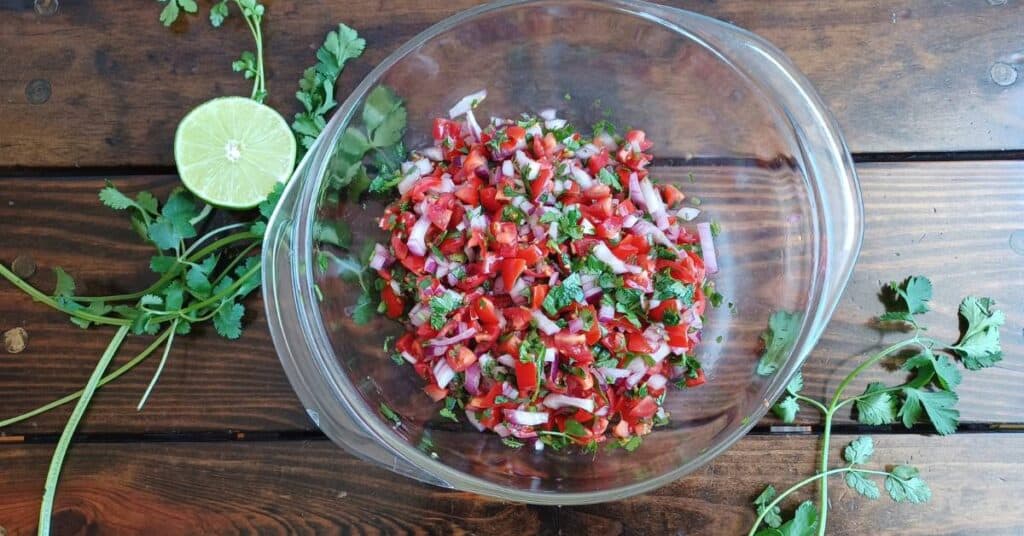 bowl of homemade pico de gallo with half a lime and cilantro around it