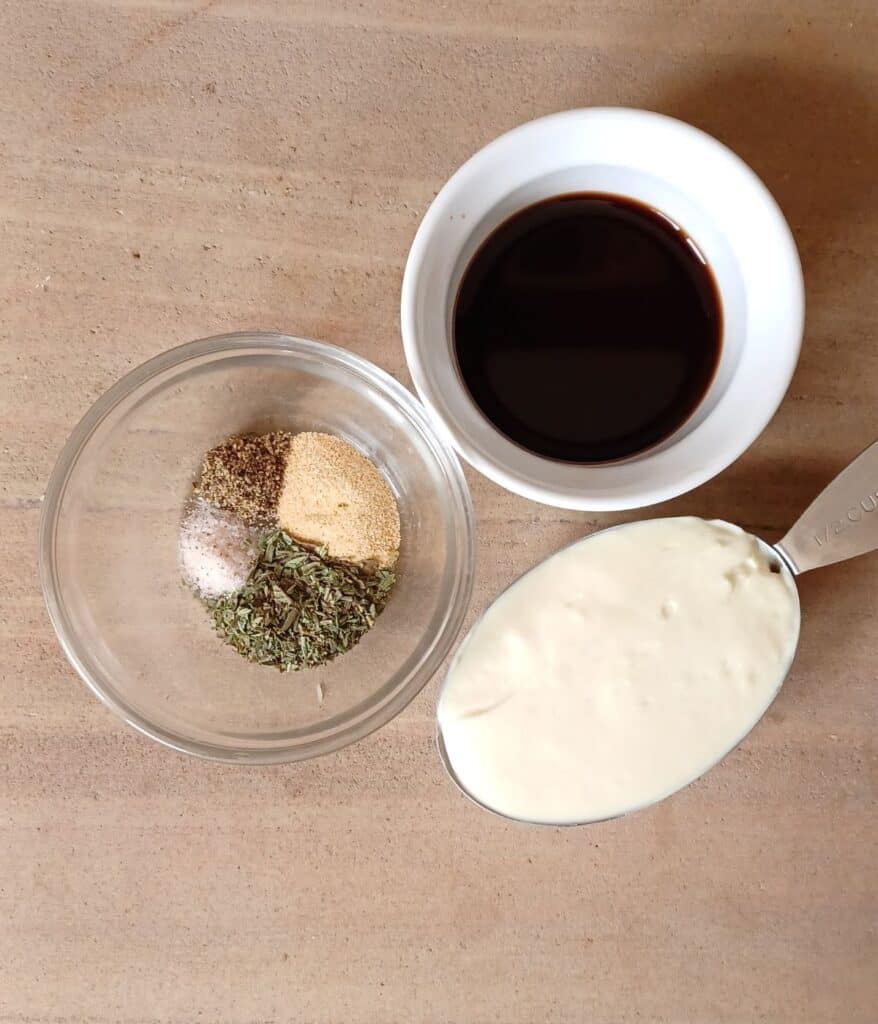 Avocado oil mayonnaise in measuring cup, balsamic vinegar in white bowl, and garlic powder, Italian herds, salt, and pepper in small glass bowl.