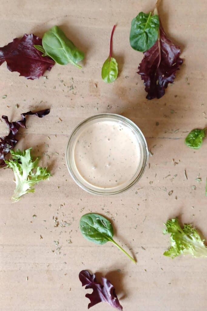 Creamy Italian dressing in a mason jar with lettuce and dried herbs sprinkled around the jar
