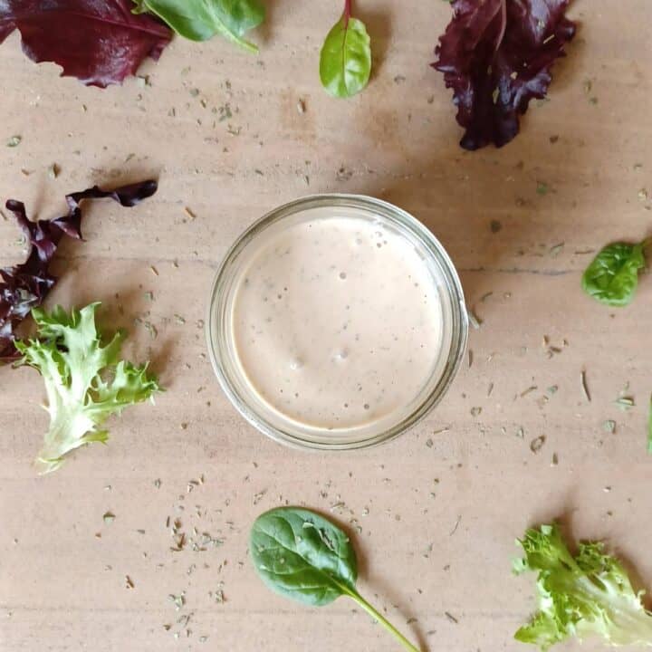 Creamy Italian dressing in a mason jar with lettuce and dried herbs sprinkled around the jar