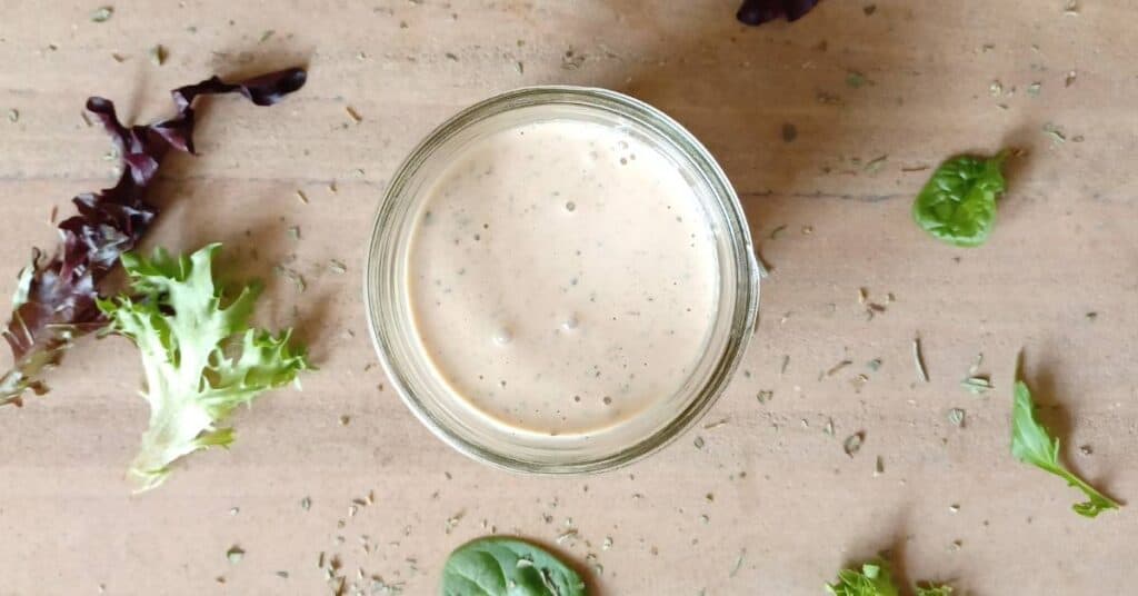 Mason jar filled with homemade creamy Italian dressing surrounded by lettuce and dried herbs