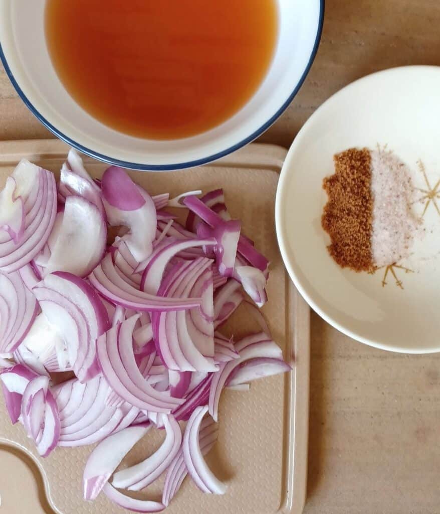 sliced red onions on cutting board, bowl of apple cider vinegar, and whit bowl with slat and coconut sugar