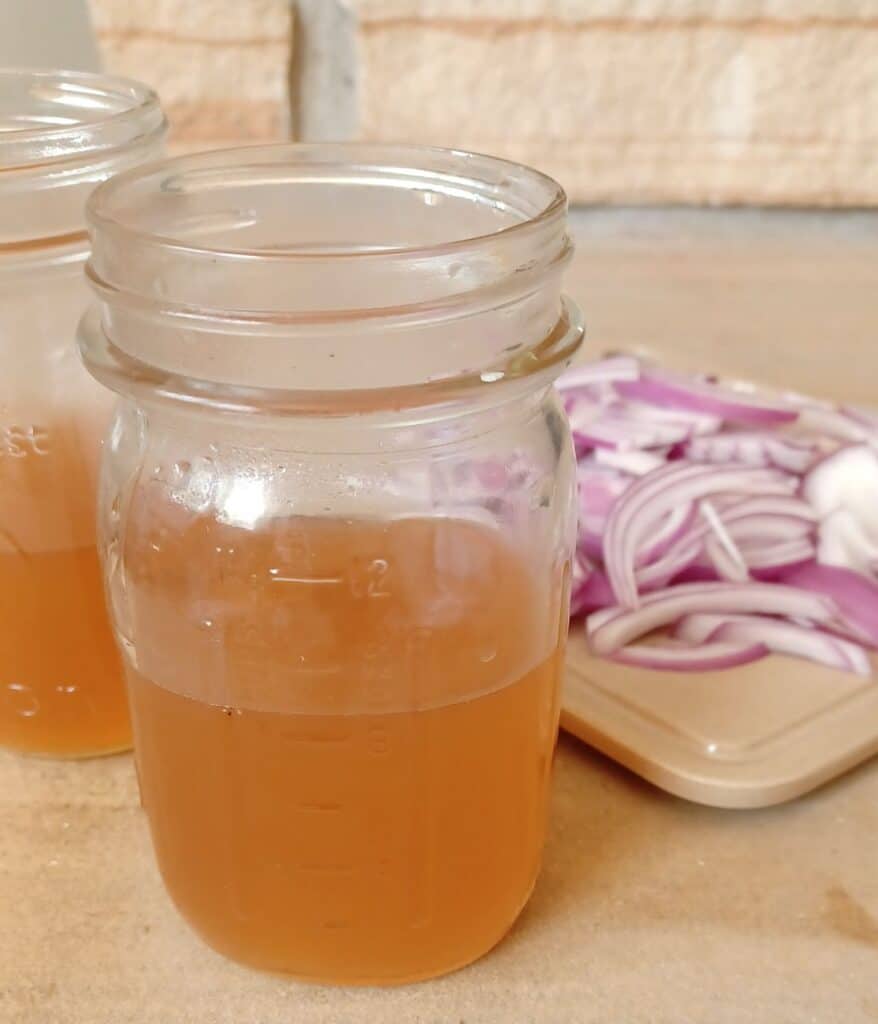Vinegar and water in 2 pint mason jars beside a cutting with sliced red onions on it.