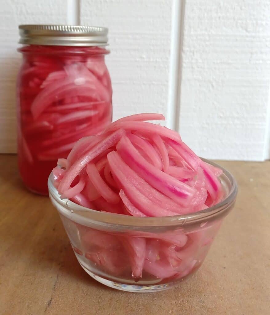 Pickled red onions in a small glass bowl and in a mason jar