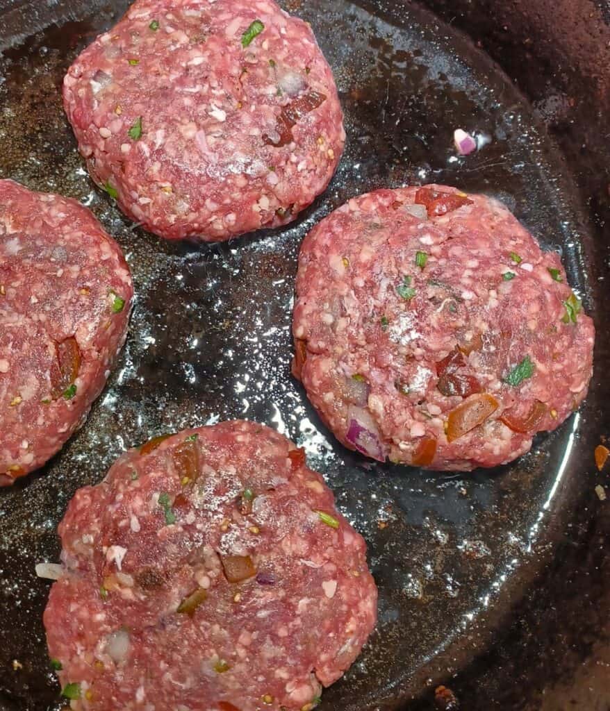 Four salsa burger patties cooking in a cast iron skillet