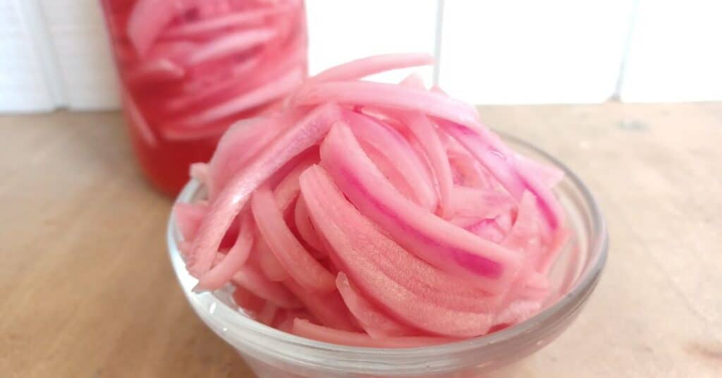 small bowl filled with pickled red onions with mason jar of onions in background